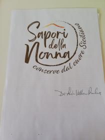 marchio è composto dalla scritta marrone Sapori della Nonna, scritta stilizzata con effetto pennellato in cui Sapori è posizionato marchio è composto dalla scritta marrone Sapori della Nonna, scritta stilizzata con effetto pennellato in cui Sapori è posizionato sopra con la s maiuscola, della è posizionato al centro fra le due scritte e la Nonna con la n maiuscola è posizionata sotto. Il gambo della N si prolunga in un elemento grafico rotondo che accerchia la scritta. Sopra la scritta Sapori vi è un elemento grafico che rappresenta l Etna una cima che parte dalla a della scritta sapori e termina sulla i finale. Fa parte del logo anche la scritta conserve dal cuore siciliano che parte dalla N e segue la curva del cerchio. Il marchio è composto dalla scritta marrone Sapori della Nonna, scritta stilizzata con effetto pennellato in cui Sapori è posizionato